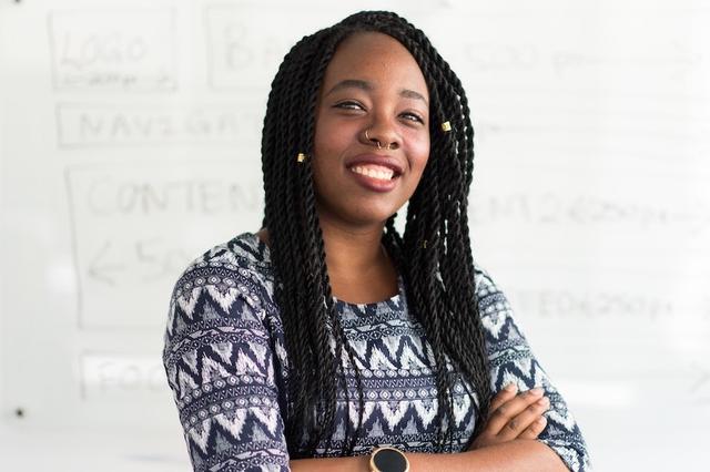 A smiling Houston teacher stands in front of a classroom whiteboard
